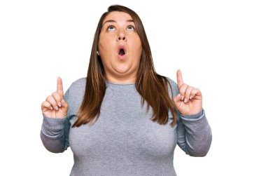 Güzel esmer ve cüsseli kadın gündelik giysiler giyip şaşkın şaşkın yukarı bakıyor, parmaklarıyla işaret ediyor ve kollarını kaldırıyordu.. 