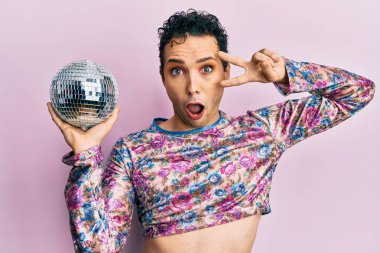 Yakışıklı adam makyaj yapıyor. Parlak disko topunu yüzünde tutuyor. Şüpheci ve alaycı görünüyor. 