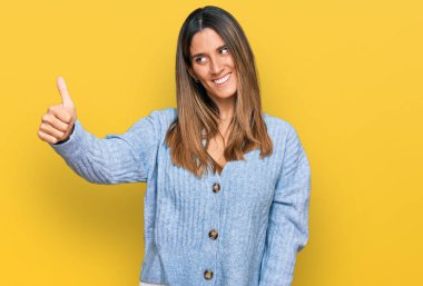 Gündelik kıyafetler giyen, gururlu görünen, gülümseyen genç bir kadın yan tarafa baş parmak hareketi yapıyor. 