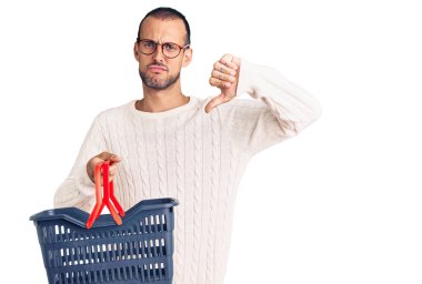 Elinde kızgın yüzüyle süpermarketten alışveriş sepeti tutan genç yakışıklı bir adam. Negatif işaret baş parmakları aşağıda, reddedilme kavramı. 