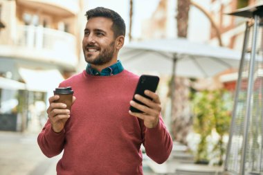 Genç İspanyol adam akıllı telefon kullanıyor ve şehirde kahve içiyor..