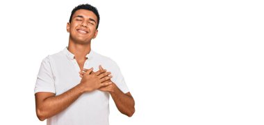 Gündelik kıyafetler giyen genç Arap adam elleri göğsünde, gözleri kapalı ve yüzünde minnet dolu bir jest ile gülümsüyor. sağlık kavramı. 