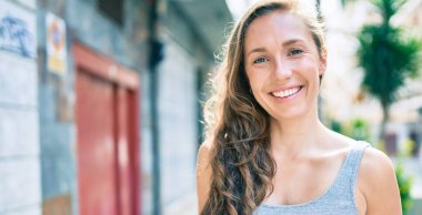 Genç sarışın kadın gülümsüyor. Şehrin caddesinde mutlu bir şekilde yürüyor.