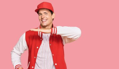 Beyzbol üniforması giyen yakışıklı beyaz adam. Elleriyle işaret ediyor. Büyük ve büyük beden işareti, ölçü sembolü. Kameraya bakıp gülümsüyor. ölçüm kavramı. 