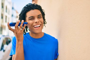 Genç Afrikalı Amerikalı adam şehrin caddesinde akıllı telefon kullanarak sesli mesaj dinliyor..