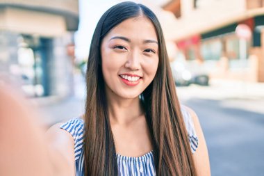 Genç Çinli kadın gülümsüyor. Şehrin caddesindeki kameranın önünde selfie çekiyor..