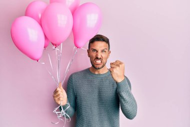 Elinde pembe balonlar tutan yakışıklı adam öfkeyle bağırıyor, öfkeyle bağırıyor ve el kaldırıyor. 