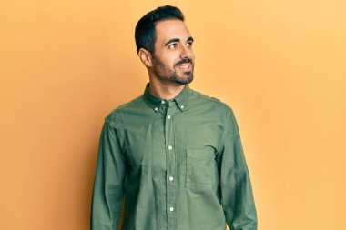 Latin kökenli genç bir adam günlük giysiler giyiyor, rahat bir görünüm takınıyor, doğal bir yüz ifadesi ve kendinden emin bir gülümsemeyle poz veriyor.. 