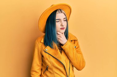 Young modern girl wearing yellow hat and leather jacket touching painful neck, sore throat for flu, clod and infection 