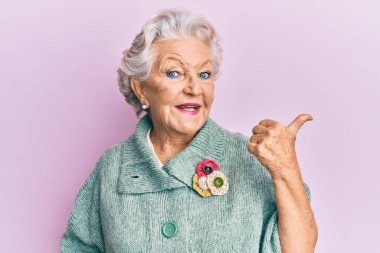 Kıdemli gri saçlı kadın, günlük kıyafetler giyip baş parmağını kaldırıyor ve ağzı açık gülümsüyor. 