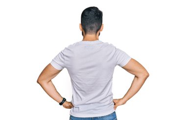 Sakallı, sıradan beyaz tişörtlü genç adam kolları vücudunda geriye doğru bakıyor. 