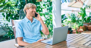 Evde çalışan orta yaşlı yakışıklı bir adam bilgisayar kullanıyor ve telefonda konuşuyor.