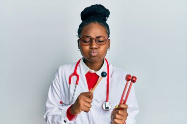 Genç Afro-Amerikan kadın doktor üniforması giyiyor elinde çatal çatal şişiren komik bir yüz var. Ağzı havayla şişer, havayı yakalar.. 