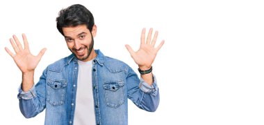 Gündelik kıyafetler giyen genç İspanyol adam on numarayı gösterip işaret ederken kendinden emin ve mutlu bir şekilde gülümsüyor.. 