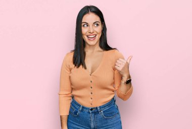 Gündelik kıyafetler giyen, gülen yüzlü genç İspanyol kadın başparmağıyla yan tarafa bakıyor ve işaret ediyor.. 