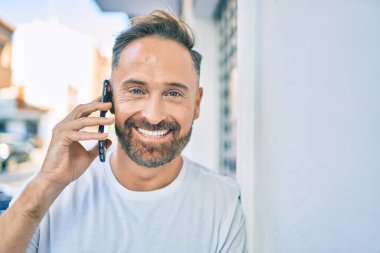 Orta yaşlı yakışıklı adam şehirde akıllı telefon kullanarak mutlu gülümsüyor..