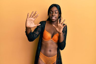 Genç Afro-Amerikalı kadın iç çamaşırı giyiyor korku ifadesinden korkuyor ve dehşete düşmüş el kol hareketi yapmayı kes, şok içinde bağırmayı kes. panik konsepti. 