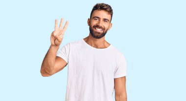 Gündelik beyaz tişört giyen genç İspanyol adam üç numarayı gösterip işaret ederken kendinden emin ve mutlu bir şekilde gülümsüyor.. 
