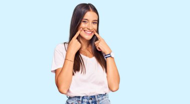 Gündelik beyaz tişört giyen genç İspanyol kadın ağzı açık gülümsüyor, parmakları işaret ediyor ve neşeli bir gülümseme sergiliyor. 