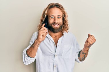 Sakallı ve uzun saçlı yakışıklı adam akıllı telefonda konuşuyor gururla bağırıyor, zaferi kutluyor ve kollarını kaldırarak başarıyı kutluyor. 