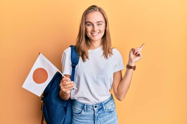 Güzel sarışın değişim öğrencisi elinde japan bayrağı ile mutlu bir şekilde gülümsüyor. 