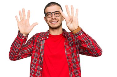 İspanyol genç adam günlük giysiler giyip dokuz numaralı parmaklarıyla işaret ederken kendinden emin ve mutlu bir şekilde gülümsüyor.. 