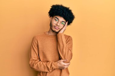 Afro saçlı, kışlık süveter giyen genç Afrikalı Amerikalı adam kollarını kavuşturup depresyondan sıkılmış ve yorgun göründüğünü düşünüyor.. 