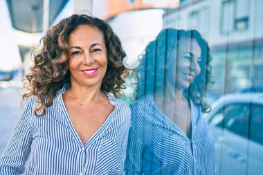 Orta yaşlı İspanyol kadın gülümsüyor. Mutlu bir şekilde şehrin duvarına yaslanıyor..