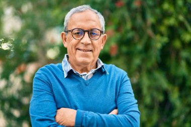 Yaşlı, gri saçlı, kollarını kavuşturmuş, gülümseyen, mutlu bir adam..