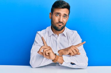 İş kıyafetleri giymiş yakışıklı İspanyol adam iki tarafı da işaret ederek masaya oturuyor. Farklı yönlerden. 