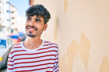 Genç İspanyol adam gülümsüyor mutlu bir şekilde şehrin duvarına yaslanıyor..