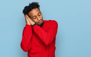 Young african american man with beard wearing casual winter sweater sleeping tired dreaming and posing with hands together while smiling with closed eyes. 