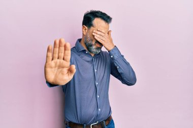 Sakallı ve gri saçlı orta yaşlı bir adam iş kıyafetleri giyiyor gözleri elleriyle kapatıyor ve üzgün ve korku ifadeleriyle jestleri durduruyor. utangaç ve olumsuz kavram. 