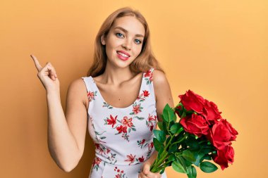 Güzel sarışın beyaz kadın elinde buket kırmızı güller tutarken mutlu bir şekilde elini ve parmağını yana doğru uzatıyordu. 