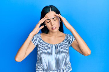 Güzel, genç bir kadın. Elleri başının üstünde, gündelik kıyafetler giyiyor. Stres yüzünden baş ağrısı çekiyor. migren ağrısı. 