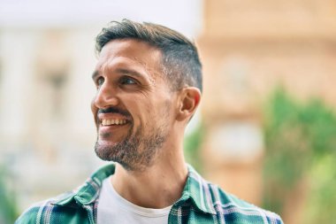 Genç beyaz adam gülümseyerek şehirde mutlu mesut duruyor..