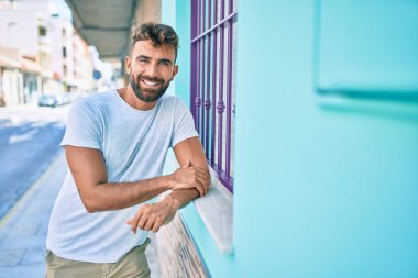 Genç İspanyol adam gülümsüyor. Mutlu bir şekilde şehrin duvarına yaslanıyor.