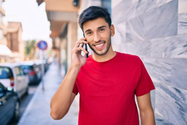 Genç Latin adam gülümsüyor ve şehirde akıllı telefondan konuşuyor..