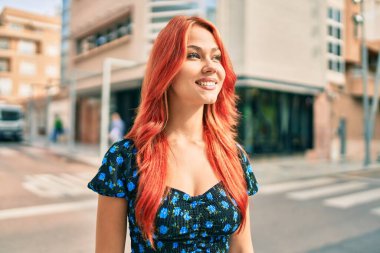 Genç kızıl saçlı kız gülümsüyor Mutlu bir şekilde yürüyor şehrin caddesinde.