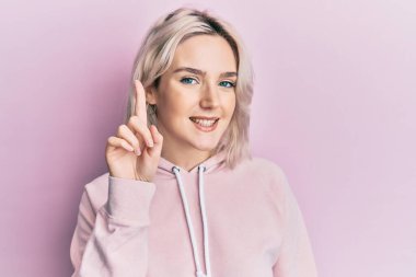 Bir fikir veya soruyla gülümseyen sıradan kıyafetler giyen genç sarışın kız mutlu bir yüzle işaret ediyor, bir numara. 