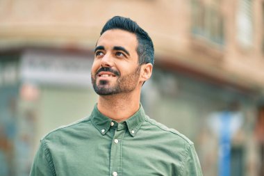 Genç İspanyol adam gülümseyerek şehirde mutlu mesut dikiliyor..