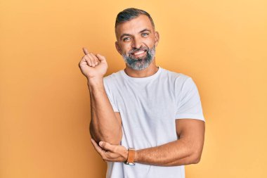 Orta yaşlı, beyaz tişörtlü, yüzünde kocaman bir gülümseme olan yakışıklı bir adam. Eli ve parmağı kameraya bakıyor.. 