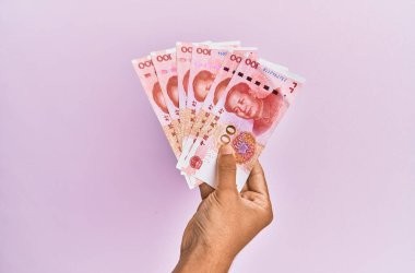 İspanyol eli 100 Yuan 'lık Çin banknotunu soyutlanmış pembe arka planda tutuyor..