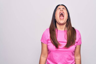 Genç, güzel, esmer, sıradan pembe tişörtler giyen bir kadın beyaz arka planda öfkeli ve sinirli bir şekilde bağırıyor. Öfkeyle bağırıyor. Öfke ve agresif kavram.