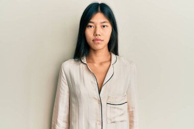 Yüzünde ciddi bir ifade olan pijama giyen genç Çinli bir kadın. Basit ve doğal bir şekilde kameraya bakıyorsun.. 