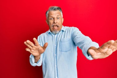 Orta yaşlı, gri saçlı, günlük kıyafetler giyen, korku ifadesinden korkan, dehşete düşmüş, elleri titreyen, şok içinde bağıran bir adam. panik konsepti. 