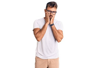 Gündelik kıyafetler ve gözlük takan genç İspanyol adam. Yüzü, depresyonu ve üzüntüyü örten yorgun eller. 