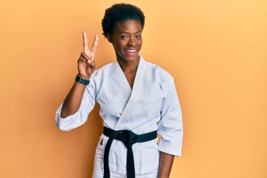 Young african american girl wearing karate kimono and black belt showing and pointing up with fingers number two while smiling confident and happy. 