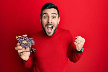 Genç İspanyol adam elinde küçük bir süpermarket arabası tutuyor gururla bağırıyor, zaferi kutluyor ve kollarını kaldırarak çok heyecanlanıyor. 