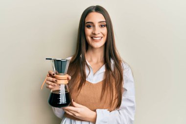 Güzel esmer, elinde çözünür kahve makinesi olan genç bir kadın pozitif ve mutlu görünüyor ve kendine güvenen bir gülümsemeyle dişlerini gösteriyor. 